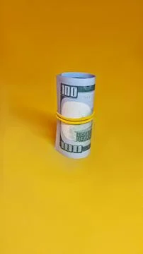 Rolled bundle of one hundred dollar bills secured  isolated on yellow background Stock Photos