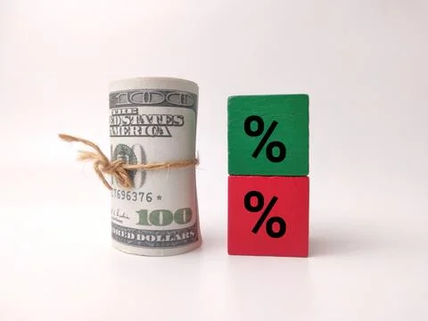 A rolled bundle of US dollar bills tied with twine stands next to stacked g.. Stock Photos