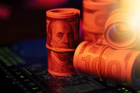 Rolled dollar bills on a screen of green financial data in red light 스톡 사진