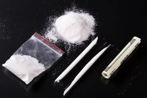 Rolled hundred dollars banknote, two lines and plastic packet of cocaine on blac Photos