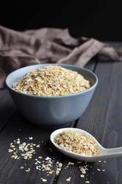 Rolled oats in ceramic bowl and spoon on dark wooden table with texture Stock Photos