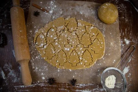 In the rolled out layer of dough, many Christmas trees are cut out, which are Stock Photos