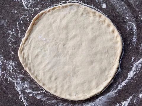 Rolled out pizza dough on floured slate surface, photographed overhead Stock Photos