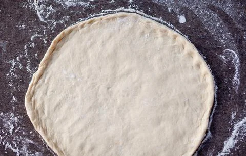 Rolled out pizza dough on floured slate surface, photographed overhead Stock Photos