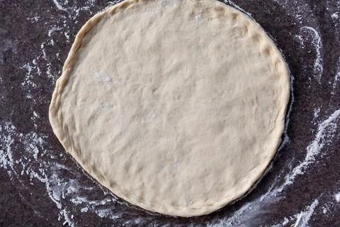 Rolled out pizza dough on floured slate surface, photographed overhead Stock Photos