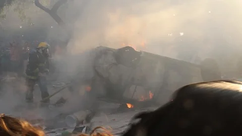 Rolled over car on fire put out by firefighters during violent fiery riots Vidéo 127199521