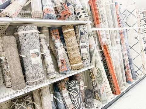 Rolled rugs of various patterns and colors displayed on shelves in a retail.. Stock Photos