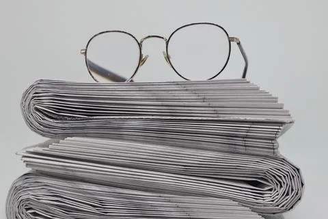 Rolled up stack of fresh newspapers and glasses, news, printed background. Stock Photos