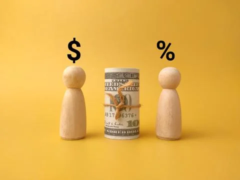 A rolled US dollar bill stands between two wooden figures with dollar and p.. Stock Photos