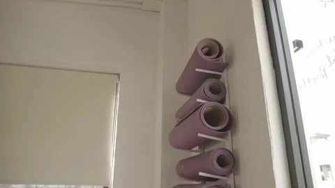 Rolled yoga mats stacked on wall rack inside fitness studio Stock Footage 334412871