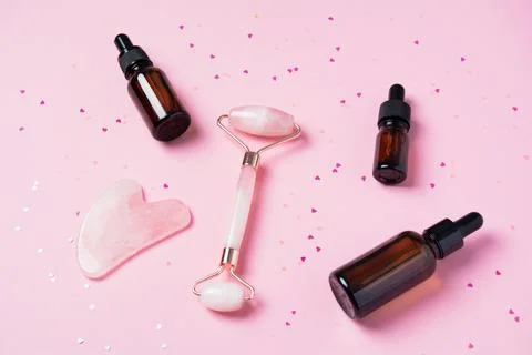 Roller and gua sha massage scraper and cometic products on a pink background Stock Photos