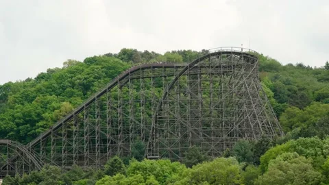 A roller coaster on a forested hill thrills screaming riders at an Video stock 192291713