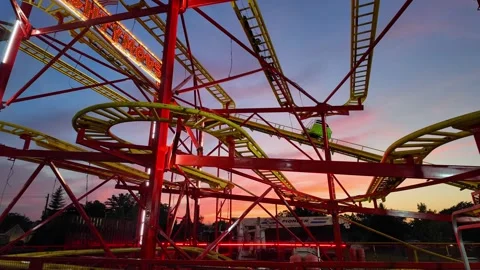 Roller coaster ride moving on tracks during an amusement park festival at sunset Stock Footage 344021479