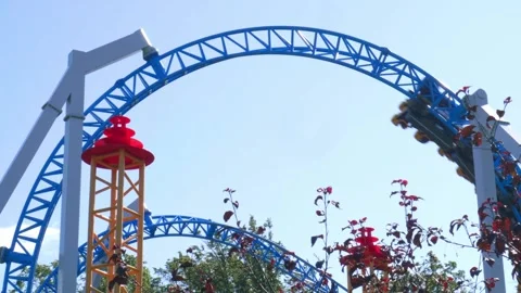 Roller Coaster Track Twists Above Vibrant Amusement Park Foliage on a Clear Day Stock Footage 312566220