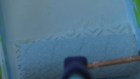 The roller is dipped in blue paint, rolled in a cuvette and painted on the wall Stock Footage 113788911