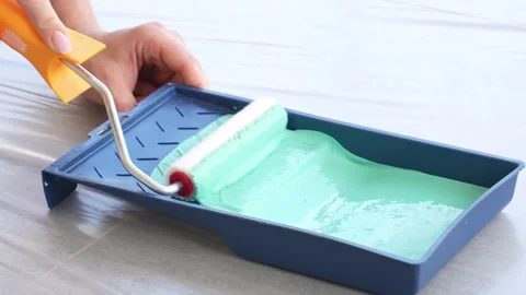 The roller picks up green paint from a container or tray. Stock Footage 252736046