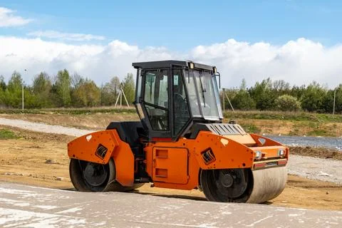 A roller is resting on a dirt road at a construction site near green trees .. 스톡 사진