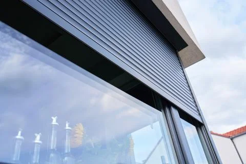 Roller shutter partly covers modern house window, with clouds reflected in .. Stock Photos