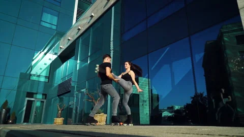 Roller skaters performing extreme stunts against glass building Stock Footage 144191199