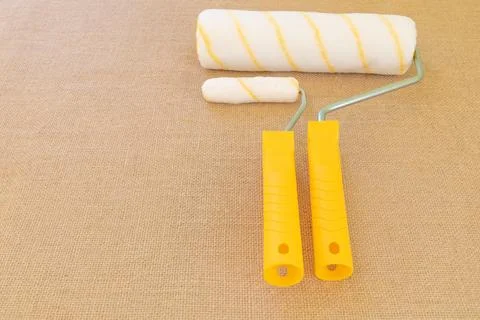 A roller with a yellow handle and a small one on a rustic fabric background Photos