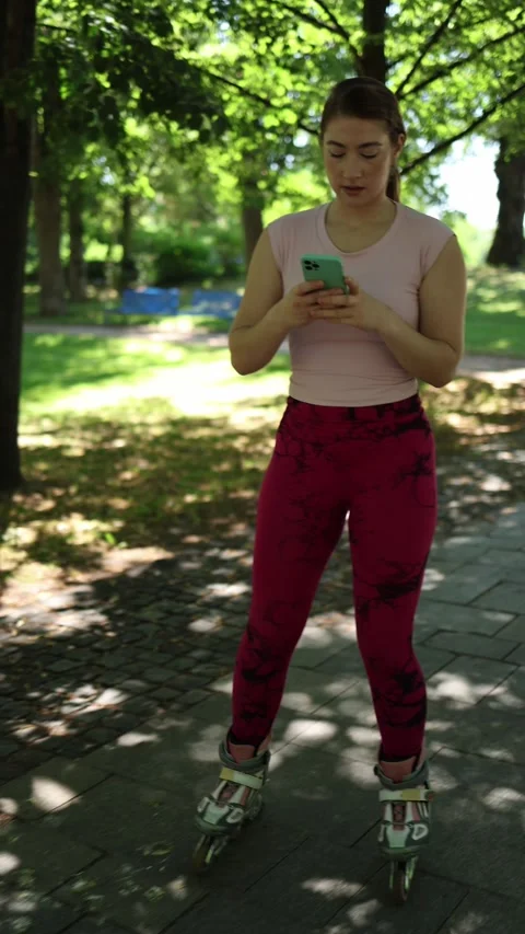Rollerblading woman stops in park to type a message on smartphone Vidéo 341476317