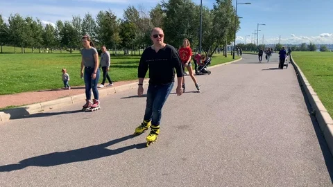 Rollers - a guy and two girls ride in the park Stock Footage 115700200