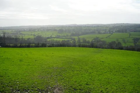 Rolling Green Fields And Distant Village Under Cloudy Sky, Wessington, England. Stock Photos