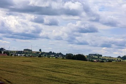 Rolling green fields under a dramatic cloudy sky, overlooking a distant villa Stock Photos