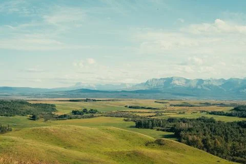 Rolling green hills and distant mountains under a bright blue sky view. Stock Photos