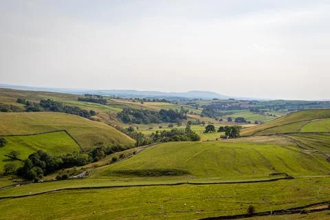 Rolling green hills with patchwork fields under a hazy sky, depicting rural.. Stock-Fotos
