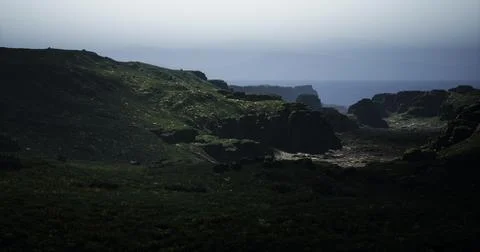 Rolling green hills stretch towards the horizon, fading into a gray ocean Stock Illustration