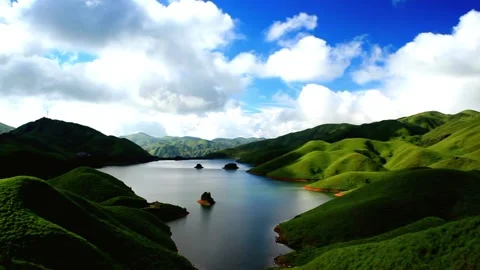 Rolling green hills surround a tranquil lake under a cloudy blue sky Video stock 311817451