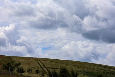 Rolling green hills under a dramatic sky with fluffy white and grey clouds 写真素材