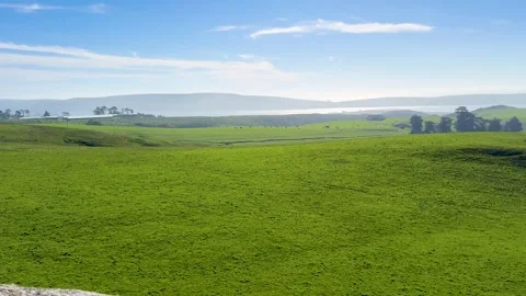 Rolling Green Pastures and Distant Cliffs Under Blue Sky Stock Footage 306251260