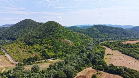 Rolling hills and green landscape with a road in the distance during daytime in Stock Footage 345484629