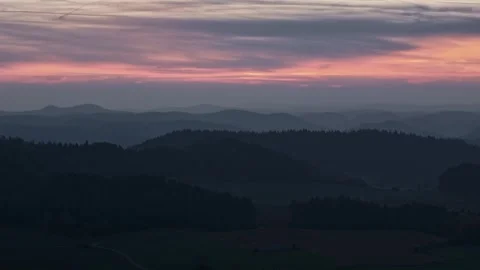 Rolling hills under a vibrant red and purple sunset with layers of misty Stock Footage 295013324