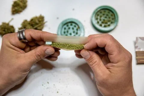 Rolling a joint with a weed bong to grind cannabis buds into the bottom. Stock Photos