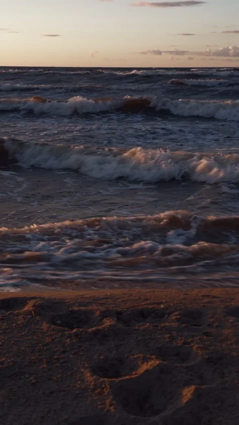 Rolling ocean waves breaking along sandy beach under warm sunset light with calm Stock Footage 346558570