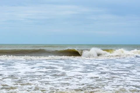 Rolling ocean waves crashing on the sandy shore under a clear blue sky Stock Photos
