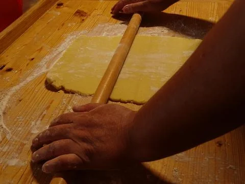 Rolling out dough by hand on a floured wooden surface in a rural kitchen Stock Photos