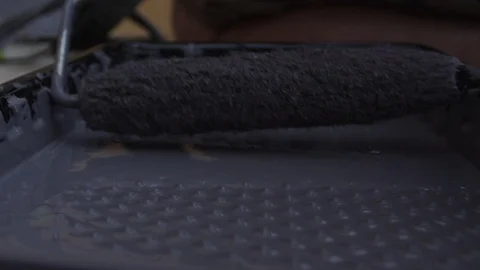 Rolling a paint roller in the paint tray to begin a remodel painting a wall Stock Footage 127598172