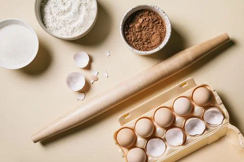 Rolling pin and baking ingredients. Flour, eggs, sugar, and cocoa powder. Stock Photos
