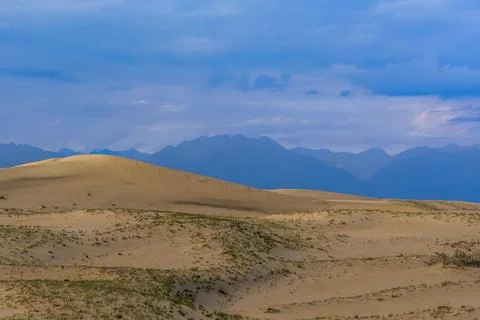 Rolling sand dunes with distant mountains under cloudy sky Stock Photos