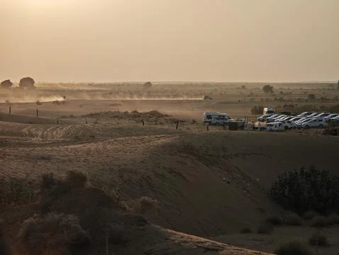 Rolling sand dunes glow under a golden sunset as vehicles kick up dust acro.. Stock Photos
