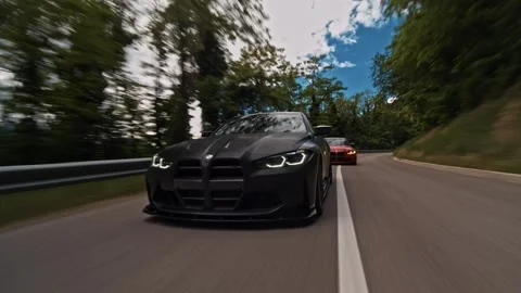 Rolling shot of a matte black bmw m4 leading a red m4 on a winding mountain road Stock Footage 328648040