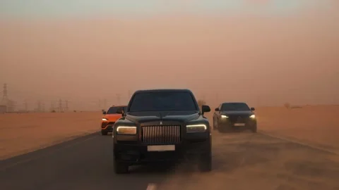 Rolling shot of Rolls Roys Cullinan Lamborghini Urus car driving in Dubai desert Video stock 200034595
