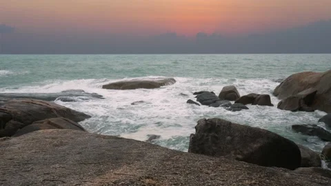 Rolling wave slamming on rocks of coastline on orange color sunset background Stock Footage 166190076