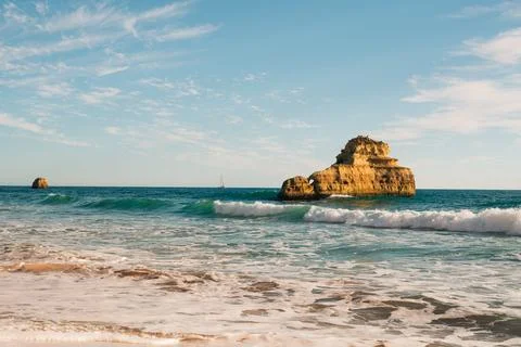 Rolling waves break gently on the sandy shore, with two isolated rock forma.. Stock Photos