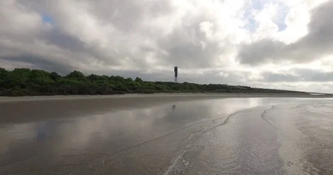 Rolling waves on a cloudy beach with lighthouse Stock Footage 76676664