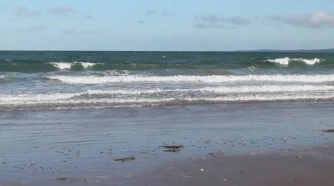 Rolling waves on seaweedy beach, bright blue sky with scattered clouds Stockbeeldmateriaal 42741251